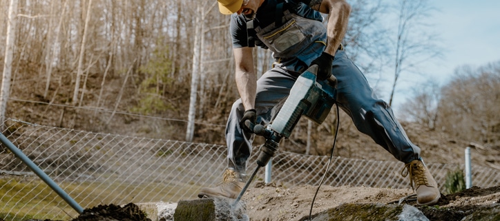 Man using a jackhammer in front of a wire fence